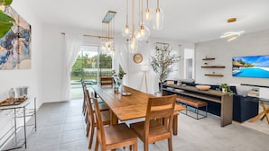 A modern kitchen with a wooden countertop, a dining area with a long table and chairs, and a living area with a sofa and TV. - Orlando Resort House: Private Pool & Themed (Kissimmee)