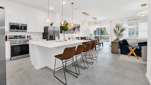 A modern kitchen with white cabinetry, stainless steel appliances, and a central island with bar stools. - Orlando Resort House: Private Pool & Themed (Kissimmee)