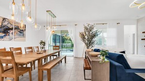 A modern dining area with a wooden table, benches, hanging pendant lights, and a view of the outdoors. - Orlando Resort House: Private Pool & Themed (Kissimmee)