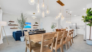 A modern kitchen with white cabinets, a dining area with wooden chairs, and hanging pendant lights. - Orlando Resort House: Private Pool & Themed (Kissimmee)