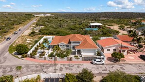 Un barrio residencial con una casa grande de techo de tejas rojas, piscina y garaje.