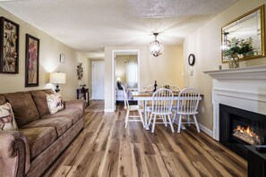 A living room with a fireplace, a dining area, and a hallway leading to another room. - Spacious Condo with Balcony Overlooking The Space Needle and downtown Gatlinburg (Gatlinburg)