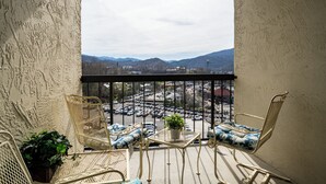 Un balcon agrémenté de meubles en osier, une petite table avec une plante, et une vue sur un parking et les montagnes.