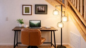 Ein Arbeitsplatz mit Laptop, Schreibtisch, Stuhl, Pflanze, Kaffeetasse und zwei gerahmten Bildern an der Wand.