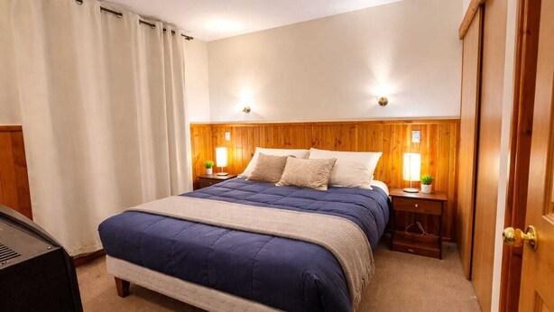 Een slaapkamer met een bed, een houten hoofdbord, nachtkastjes met lampen en een deur.