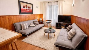 Een woonkamer met een bank, een salontafel, een televisie en een schilderij aan de muur.