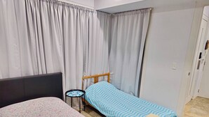 A single bed with a floral bedspread, a small bedside table with a patterned tray, and a blue-striped bedspread. - The Bella Nest - Bella Vista (Sydney)