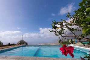 A pool with clear blue water, surrounded by greenery and a clear sky.