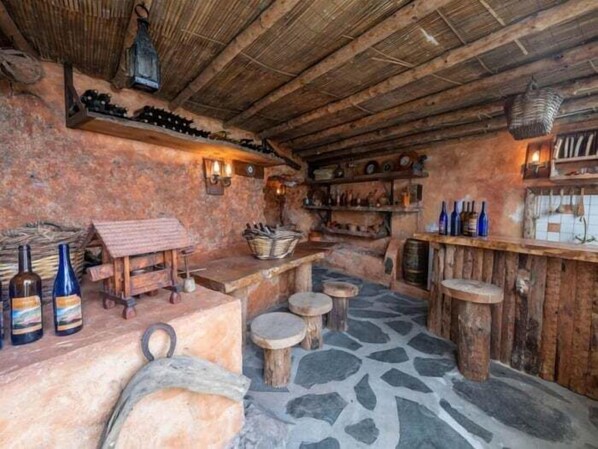 A rustic interior with stone flooring, wooden furniture, and a bar area with bottles.