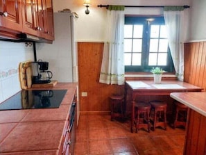 A kitchen with wooden cabinets, a coffee maker, a dining table with chairs, and a window with curtains.