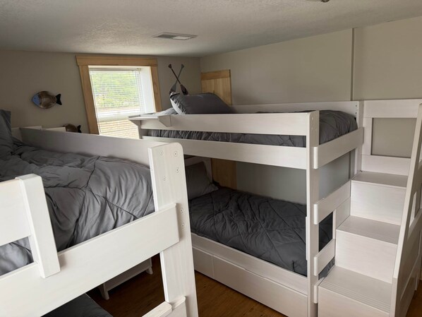 A room with bunk beds, a window with blinds, a wall decoration, and a ceiling vent.
