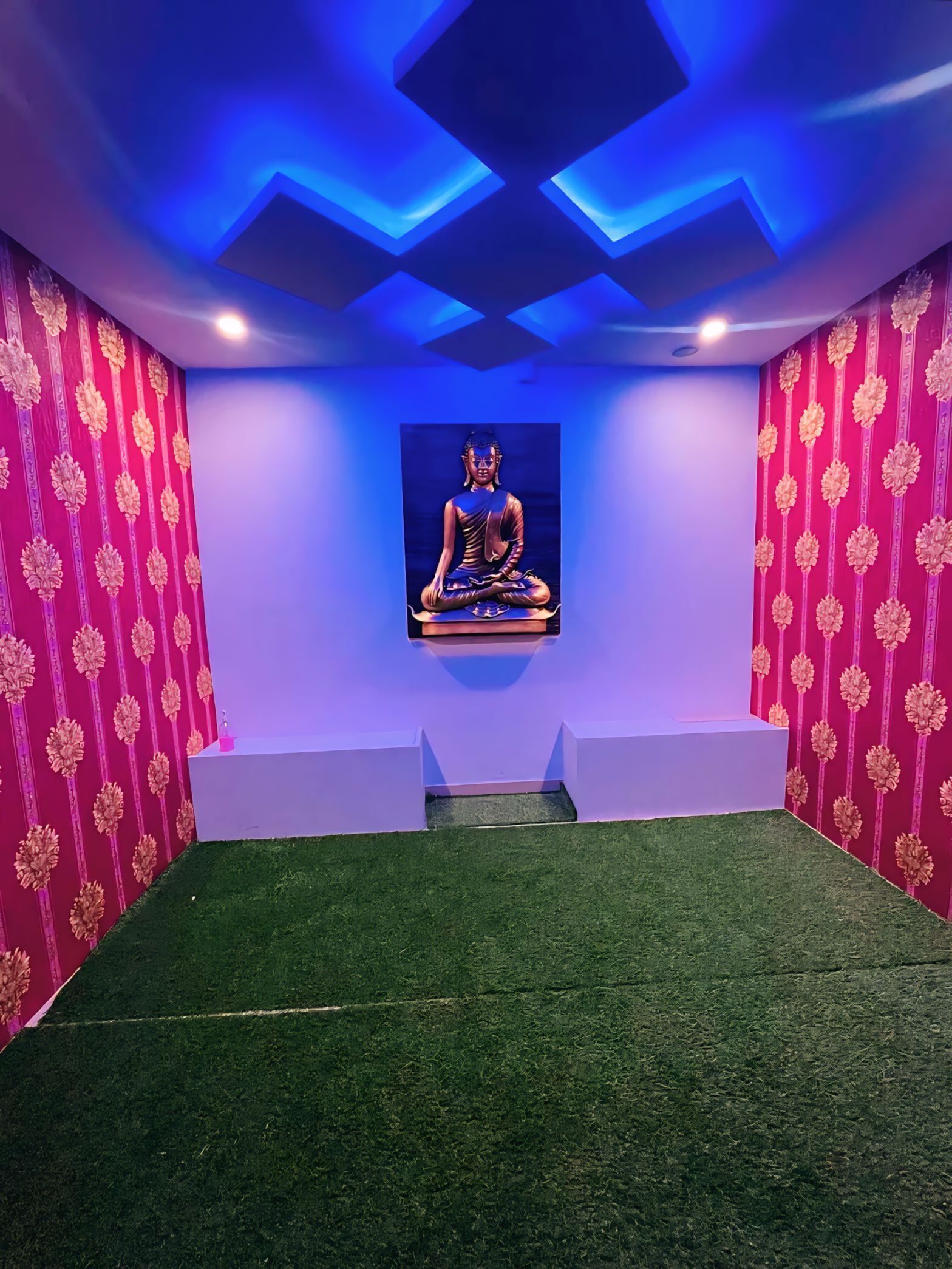 Quarto com estátua de Buda, grama sintética verde e paredes com padrão rosa.