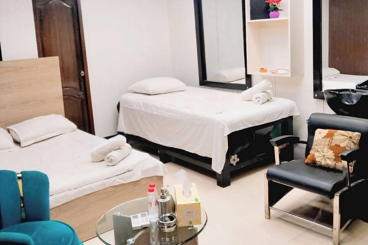 A hotel room with two beds, a glass coffee table, a blue armchair, a black chair, and a large mirror.