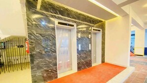 A hotel lobby with marble walls, two elevators, a red carpet, and a metal gate.