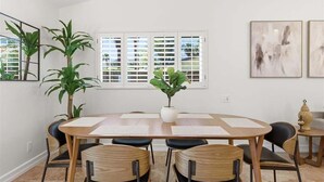 Spiseområde med et træbord, sorte stole, en potteplante og kunst på væggen.