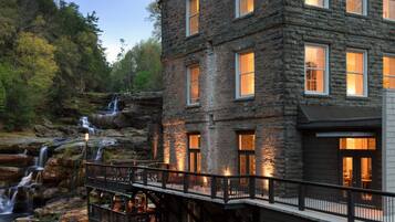 A stone building with multiple windows, a waterfall, and a wooden deck.