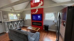 A compact living space with a sofa, a TV, a small table, and a kitchen area. - Wally’s Matchbox |New|Hot Tub|Fire Pit|Close 2 All (Hawley)