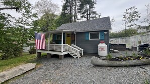 A small building with a porch, a flag, and a barrel. - Wally’s Matchbox |New|Hot Tub|Fire Pit|Close 2 All (Hawley)