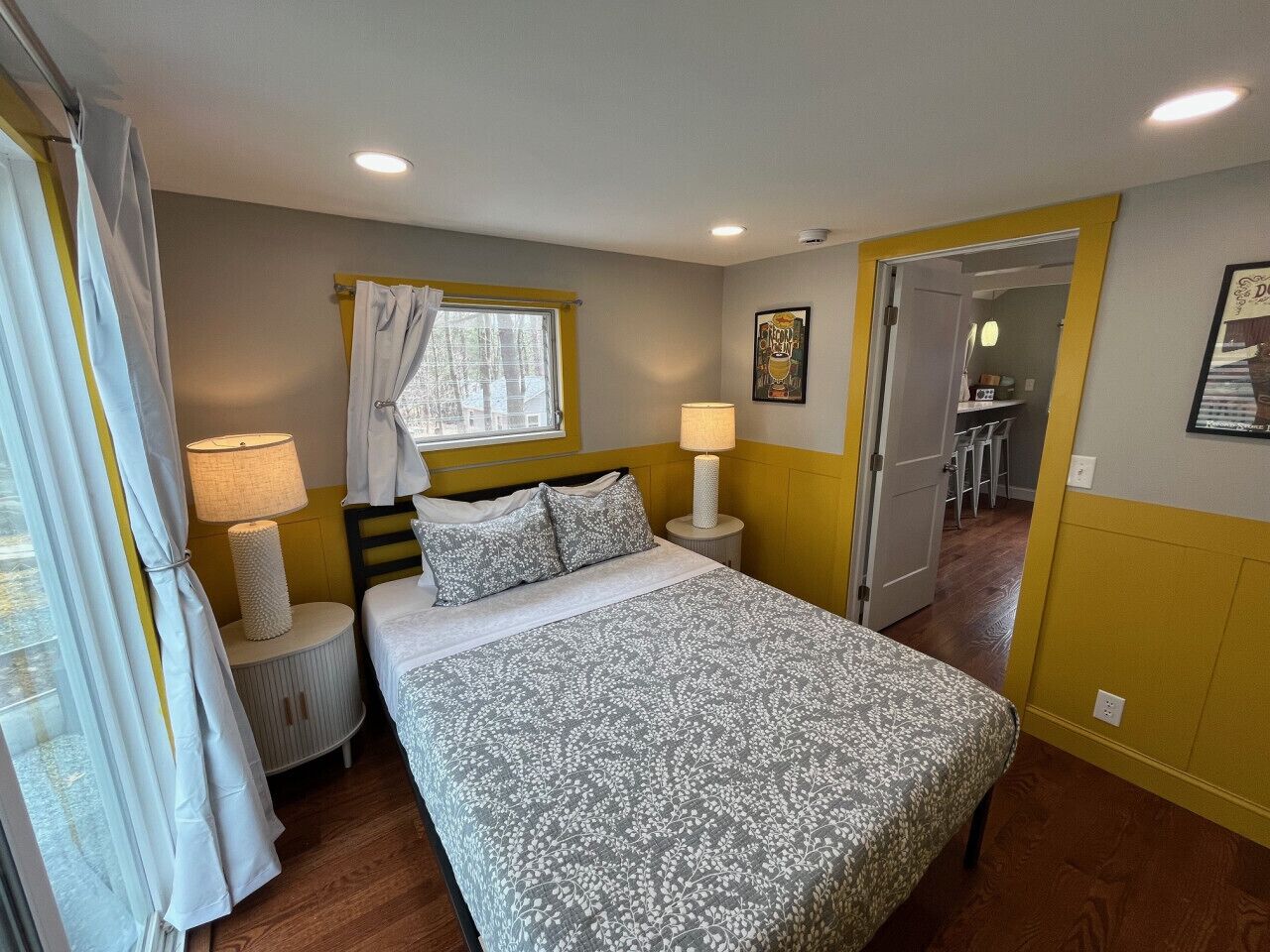 A bedroom with a bed, bedside lamps, a window with curtains, a door leading to a bathroom, and a small round table.