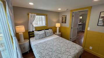 A bedroom with a bed, bedside lamps, a window with curtains, a door leading to a bathroom, and a small round table.