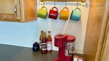 Uma bancada de cozinha com cafeteira, açúcar, xarope e canecas.