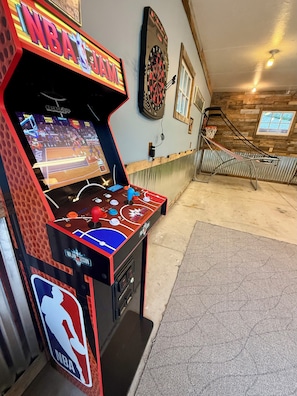 An arcade with an NBA-themed game, a dartboard, and a wooden wall.