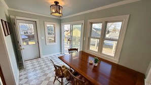 A dining area with a wooden table, chairs, a hanging light fixture, and large windows.