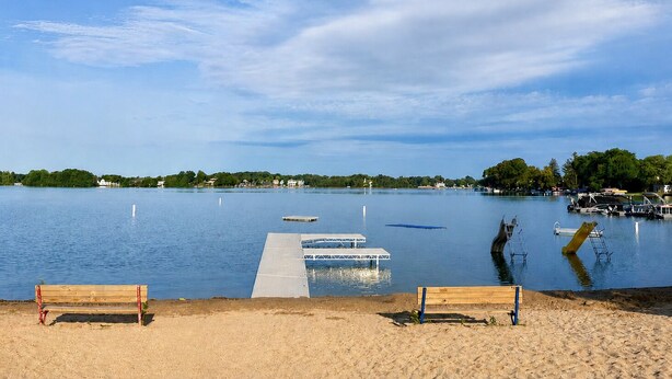 A beach with a wooden bench, a dock, and calm water.