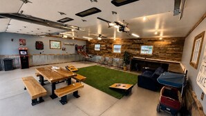 A spacious indoor area with a ping pong table, benches, a small green turf area, and a seating area with a couch and a small table.