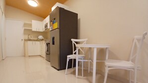 Una cocina con armarios blancos, un refrigerador, un microondas y una mesa de comedor blanca con sillas.