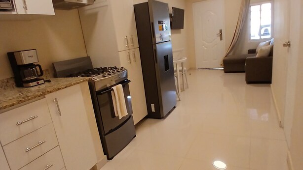 Una cocina moderna con armarios blancos, un refrigerador de acero inoxidable, una estufa a gas y una cafetera.