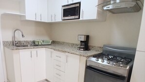 Una cocina con armarios blancos, una estufa de acero inoxidable, un microondas y una cafetera.
