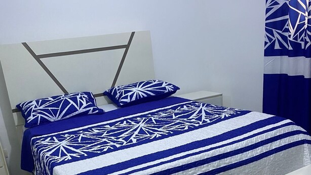 A bed with a geometric patterned bedspread, a white headboard, and a white bedside table. - Apartment in La Vega, 20 minutes from the Fula river. (Concepcion De La Vega)