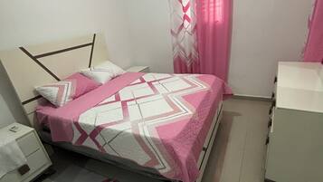 Un dormitorio con cama, mesita de noche, cómoda y ventana con cortinas.