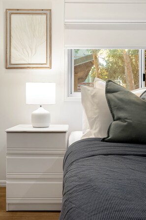 A bedroom with a bed, a bedside lamp, a window, and a framed artwork on the wall. - Sandcastle House - Sleeps 12 steps from the beach (Point Lookout)