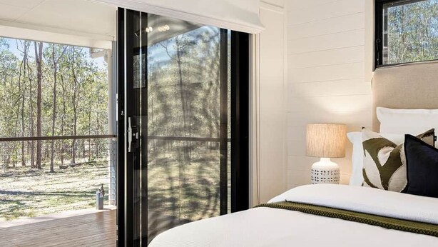 A bedroom with a large bed, a nightstand, a lamp, and a view of a deck and trees.