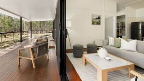 A modern living room with a sofa, coffee table, and ottomans, a large window, and a view of the outdoors.