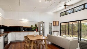 A modern kitchen with wooden cabinets, a dining table with chairs, and a large window with a view of trees.