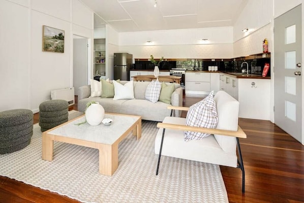 A modern living room with a sofa, ottomans, a coffee table, and a kitchen in the background.