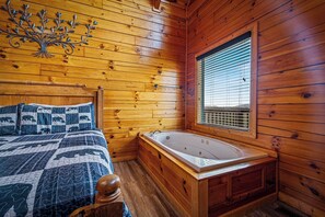 Ein Holzhütten-Zimmer mit Bett, einem Fenster mit Jalousien und einer Badewanne.