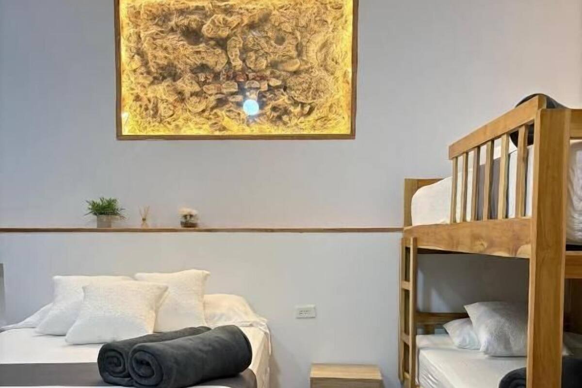 A room with a bed, a wooden bunk bed, a small table, and a wall-mounted artwork.