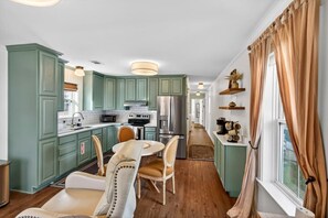 A kitchen with teal cabinets, a dining table with chairs, and a refrigerator. - Tiny Tide Cottage· Golf Cart Add · Stroll Downtown (Ocean Springs)
