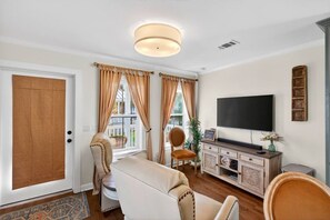 A living room with a sofa, chairs, a television, and a cabinet. - Tiny Tide Cottage· Golf Cart Add · Stroll Downtown (Ocean Springs)