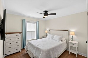 Ein Schlafzimmer mit einem Bett, Nachttischen, einem Deckenventilator und einem Fenster mit Vorhängen.