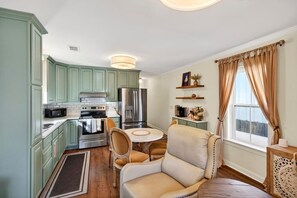 A compact kitchen with modern appliances, a dining area with a round table, and a cozy seating arrangement. - Tiny Tide Cottage· Golf Cart Add · Stroll Downtown (Ocean Springs)