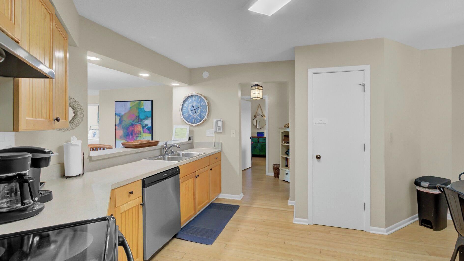 A modern kitchen with wooden cabinets, a dishwasher, and a large clock on the wall.