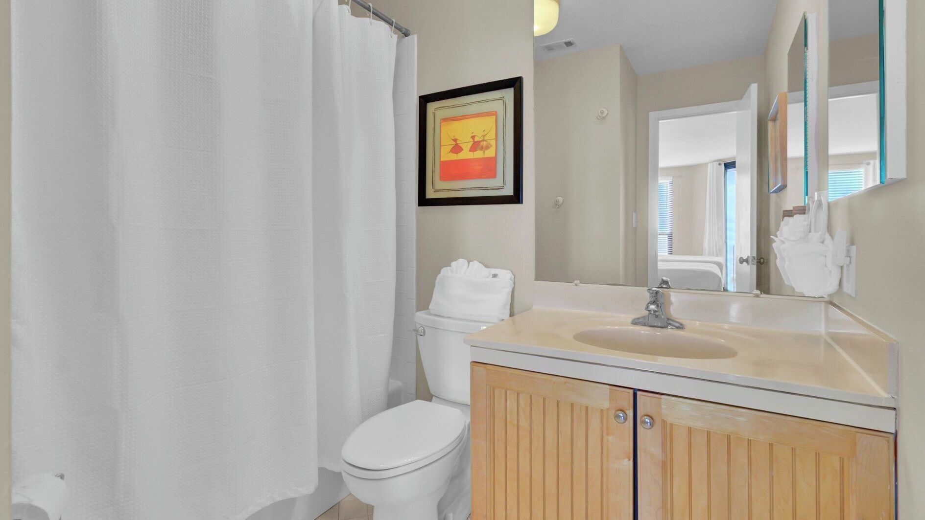 Une salle de bain avec un rideau de douche, des toilettes, un lavabo, un miroir et un tableau encadré au mur.