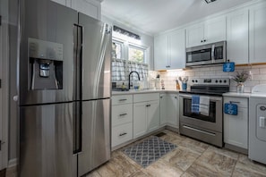 A modern kitchen with stainless steel appliances, white cabinetry, a tiled backsplash, and a window with curtains.