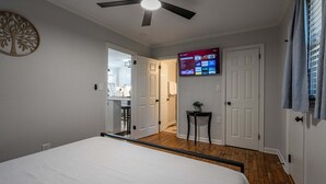 A bedroom with a bed, a ceiling fan, a TV mounted on the wall, and a door leading to a bathroom.