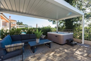 Eine Terrasse im Freien mit überdachter Sitzgruppe, einem Whirlpool und einem Blumentopf.